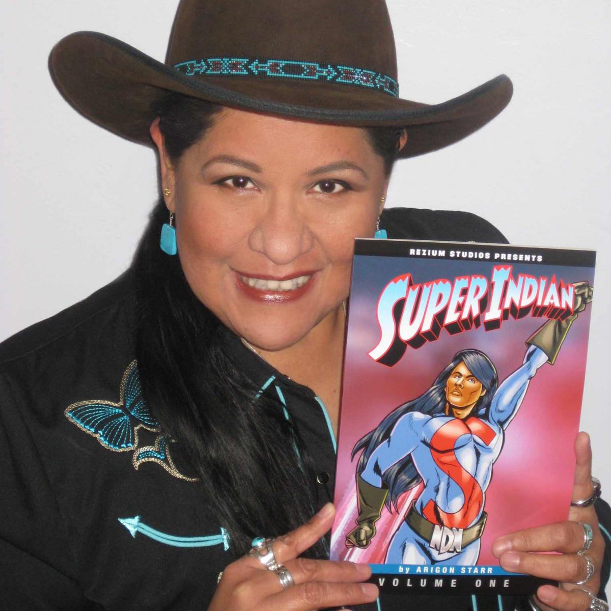 Arigon Starr in western shirt and a cowboy hat, holding a copy of her comic, "Super Indian."