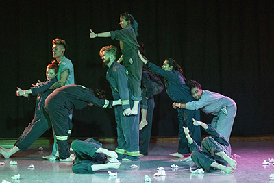 Nearly a dozen dancers, barefoot and dressed in coveralls, in a variety of modern dance poses.