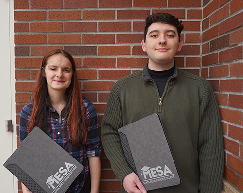 Two smiling students standing, holding MESA folios.