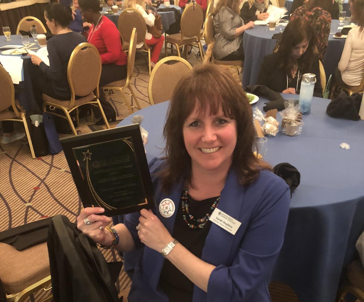 A smiling Sarah Hopkins holds up the award