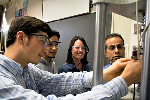 Three people observe a fourth as he handles wiring on a machine.