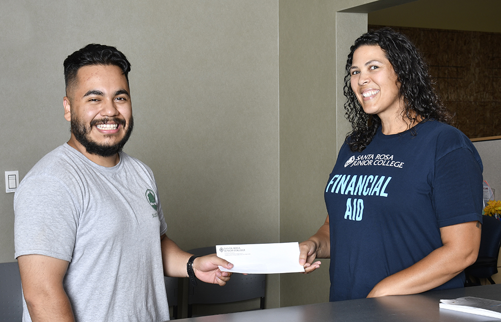 Student and financial aid worker, both smiling and holding each end of an envelope.