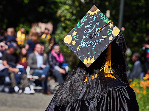 Graduate in cap and gown; handwritten message on cap reads, "It never gets easier; you just get stronger"