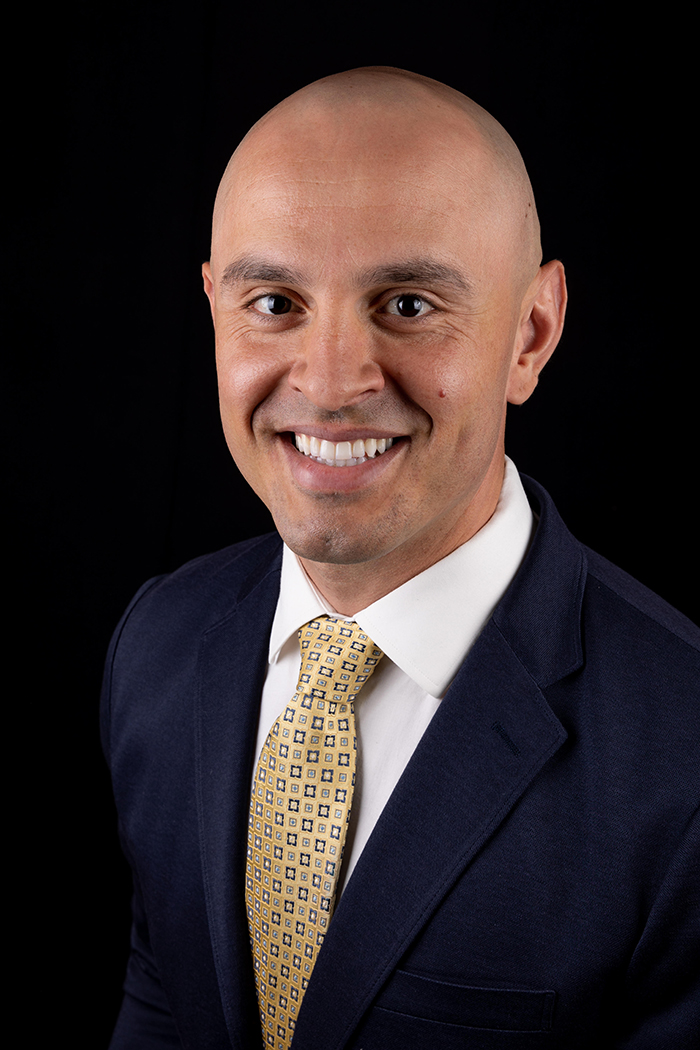 Profession head and shoulders portrait of 30-something Latinx man in dark business suit.