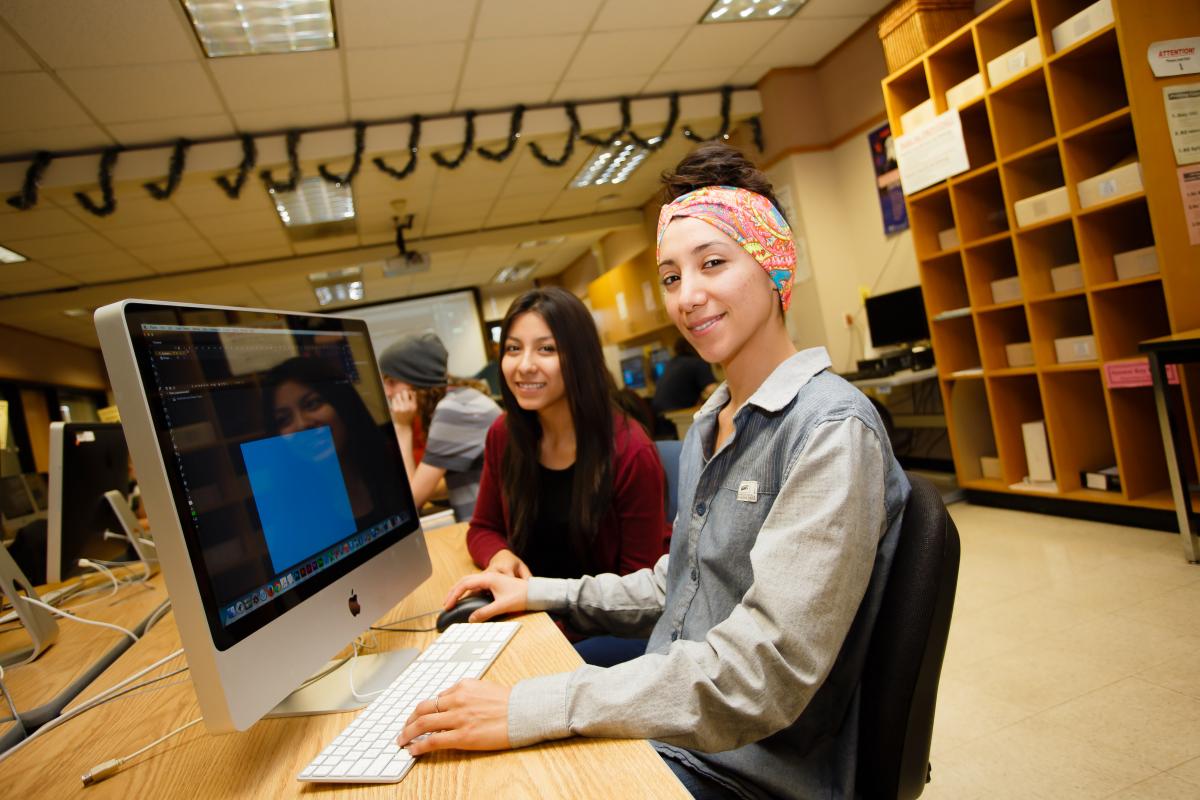 Two students at computers turn and smile at the viewer