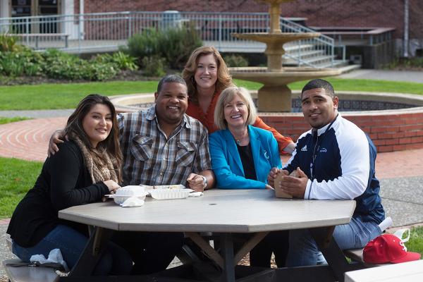 Five SRJC employees seated at a picnic table, smiling at the viewer.