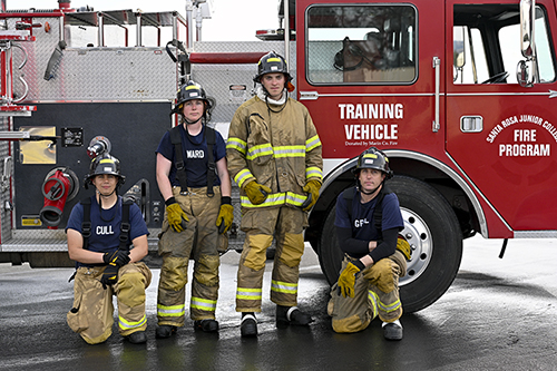 Four fire cadets in front of a training fire truck at PSTC campus.