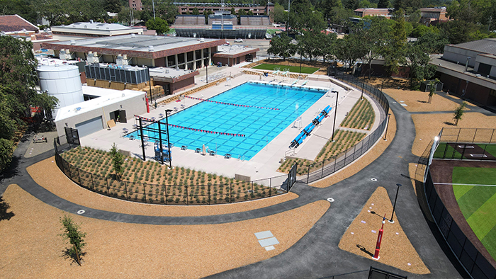 Angled arial view of sparkling blue Olympic-sized pool, surrounded by white concrete decks, semi-circular fencing, and newly planted landscaping, next to the Quinn Swim Center.