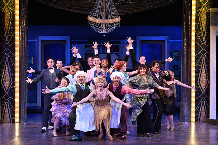 Group of actors onstage, arms oustretched, performing a musical scene.