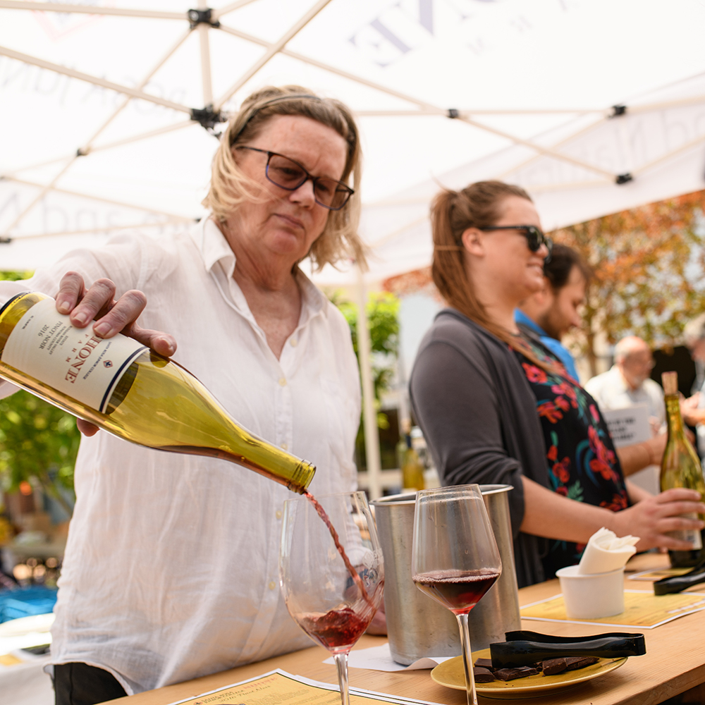 Volunteer pouring a glass of wine at the patio tasting area.